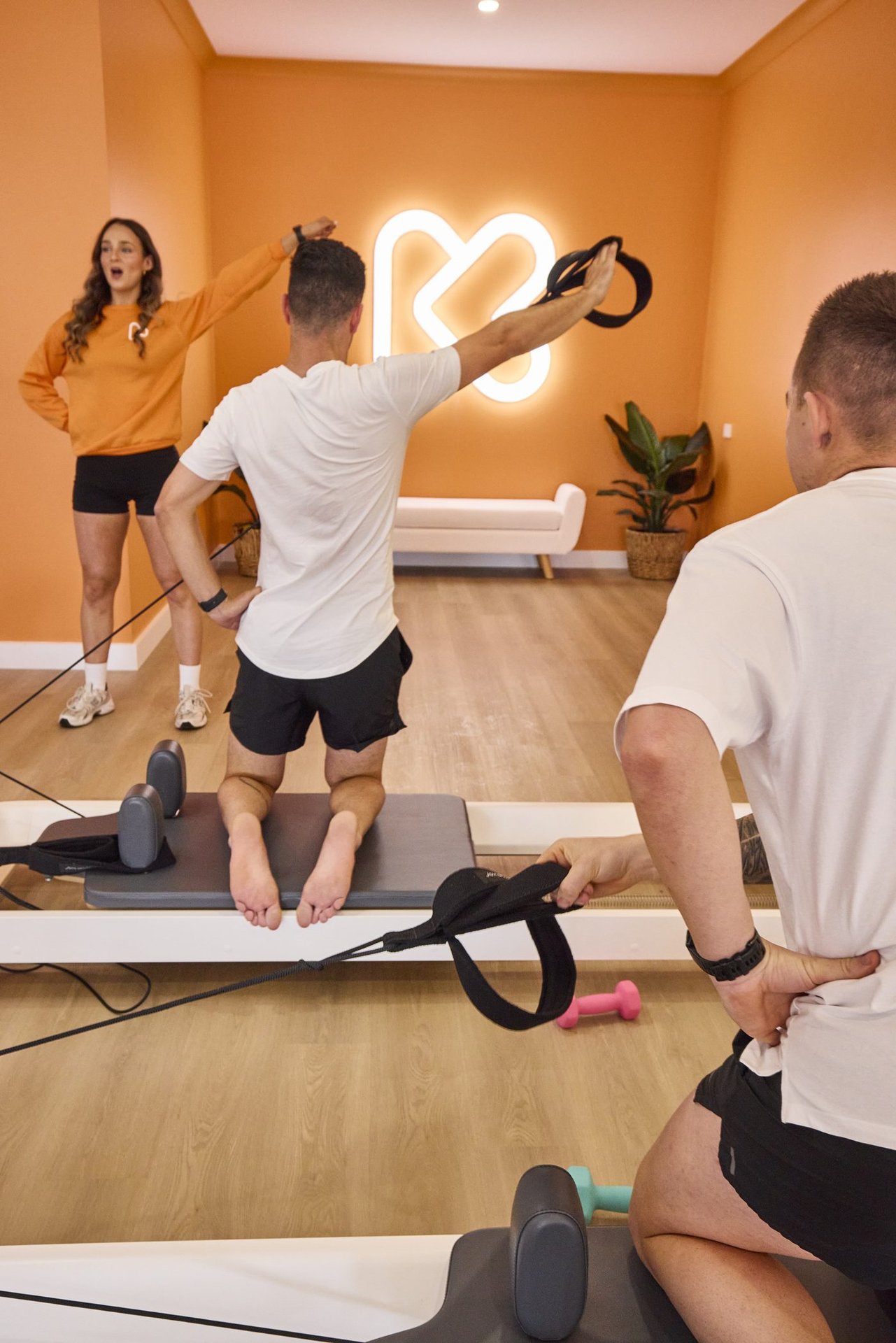 Instructor demonstrating reformer Pilates technique with neon logo in background